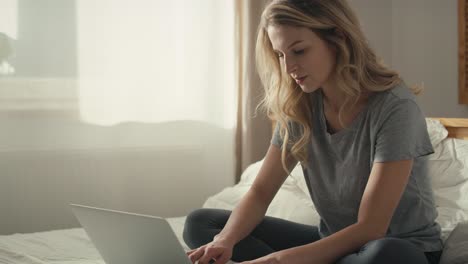 caucasian woman sitting on the bed and using the laptop at morning