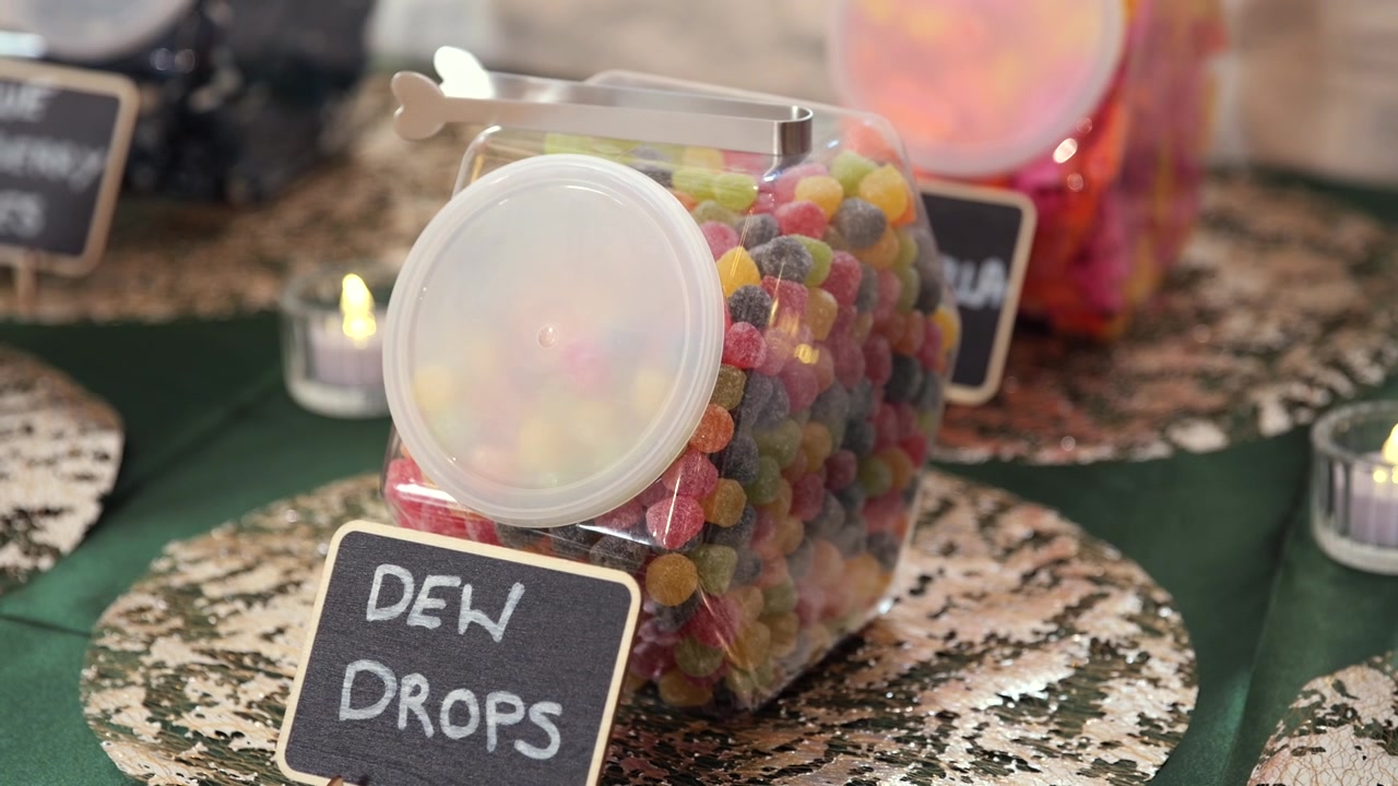 Handheld close-up of colorful dew drop candy jar on wedding sweets table.