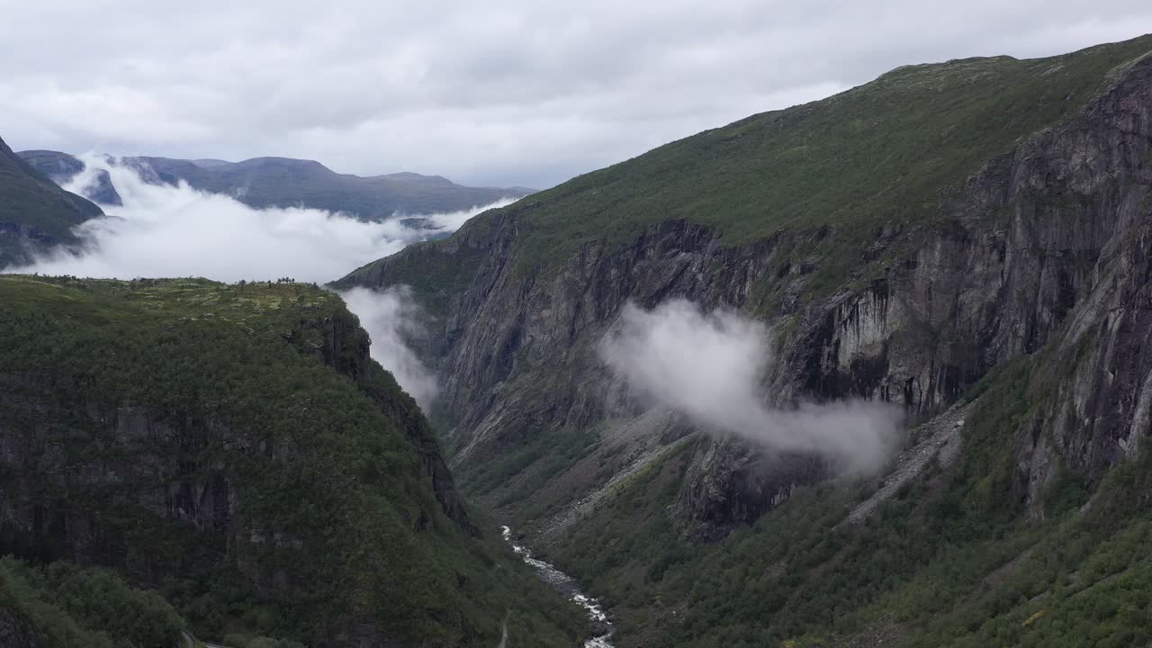 Drone glides through misty woodland valley near Vøringsfossen waterfall at the Hardangervidda Plateau, with steep cliffs and dense forest below.