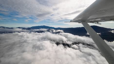 Flying over clouds and mountains, wingtip view small aircraft aviation