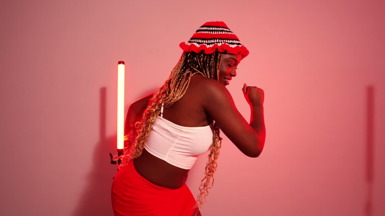 Donna con trecce e cappello con abito rosso e bianco che corre in studio