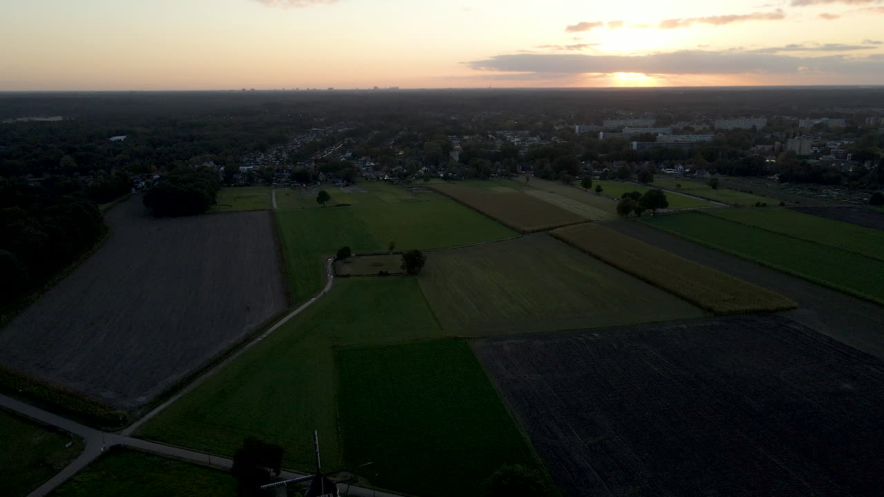 jib up of classic windmill surrounded by green meadows at sunset