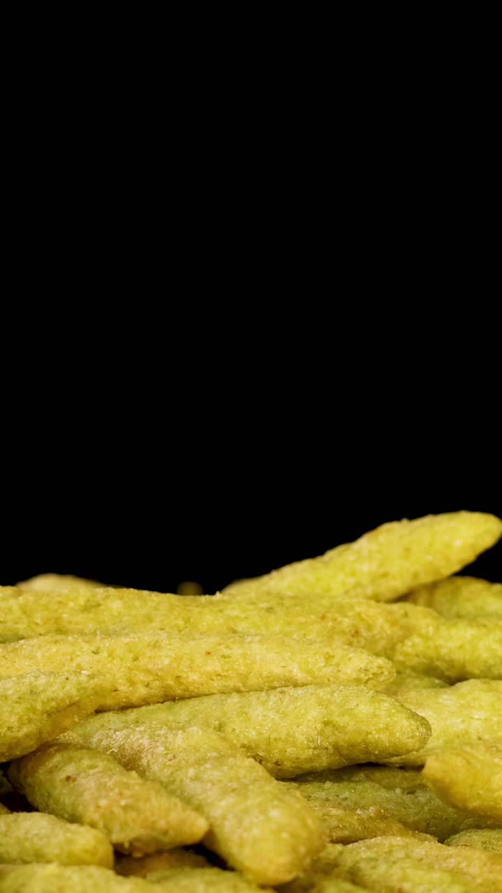 Human hand selects green pea puffed snack stick from pile, close-up, dramatic studio lighting