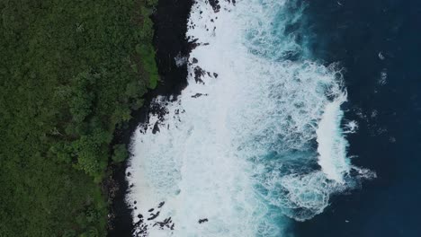 Aerial-view-of-waves-crashing-in-slow-motion-onto-a-rocky-Hawaiian-shoreline-with-lush-green-vegetation