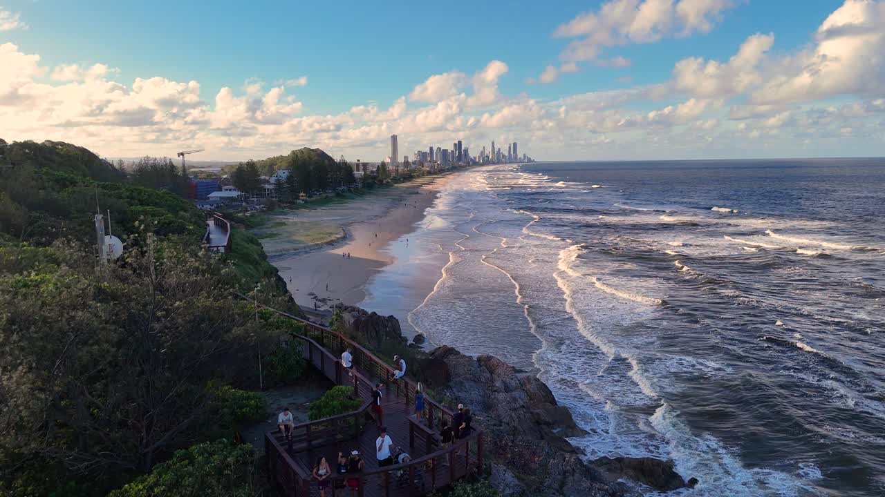 Aerial footage of Gold Coast's coastline with waves, sandy beach, and distant city skyline under a clear sky
