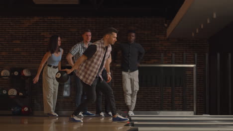 a young caucasian man makes the final throw with a bowling ball and wins the game with the support and joy of his friends of different nationalities. rejoice and celebrate the victory