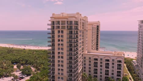 a drone shot descends over a beachfront hotel at sunset, capturing the sandy shores, ocean waves, and the hotel’s sparkling pool under a golden sky.