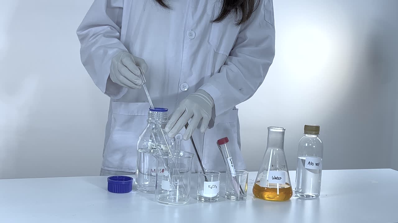 Scientist conducts a potassium carbonate experiment, mixing chemicals in a lab with controlled lighting and precise movements