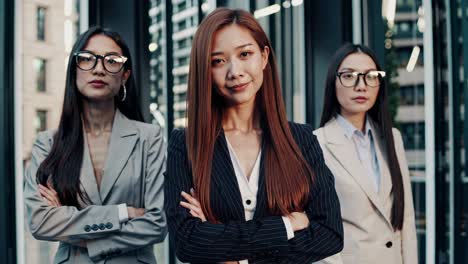 three confident businesswomen stand together with their arms crossed, exuding professionalism and determination against the backdrop of modern architecture