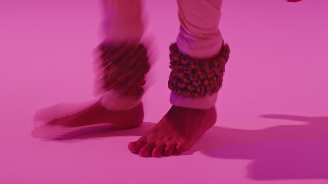 보라색 배경에 전통적인 인도 의상을 입고 춤을 추는 여성 카타크 댄서의 발과 종에 가까이 가십시오.