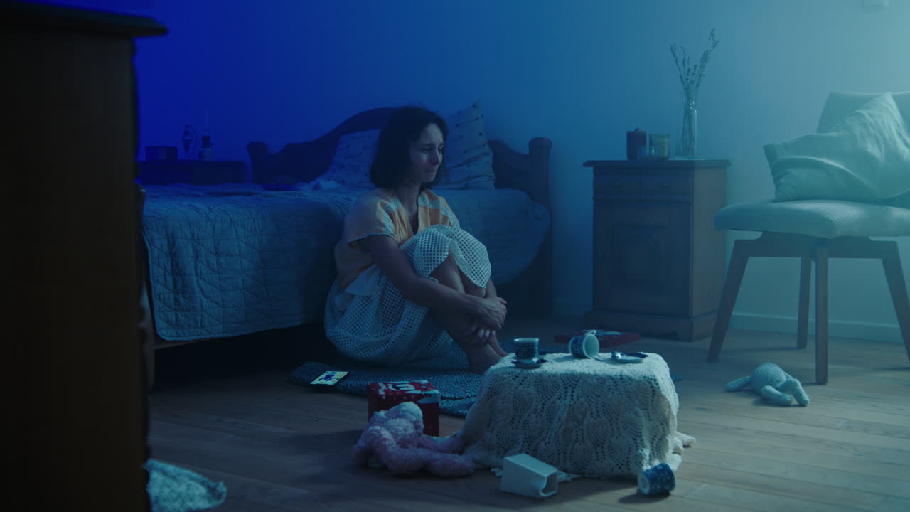 A traumatised and disoriented girl sits on the bedroom floor