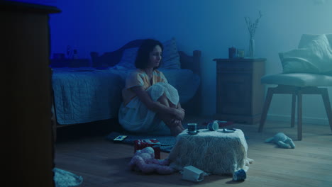 a traumatised and disoriented girl sits on the bedroom floor