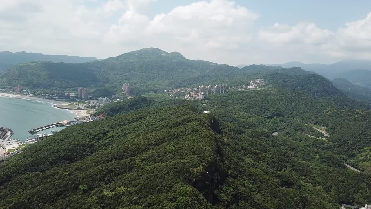 vista aérea de los acantilados boscosos en el norte de taiwán bajo un cielo nublado con el puerto y la costa de giuhou en el fondo