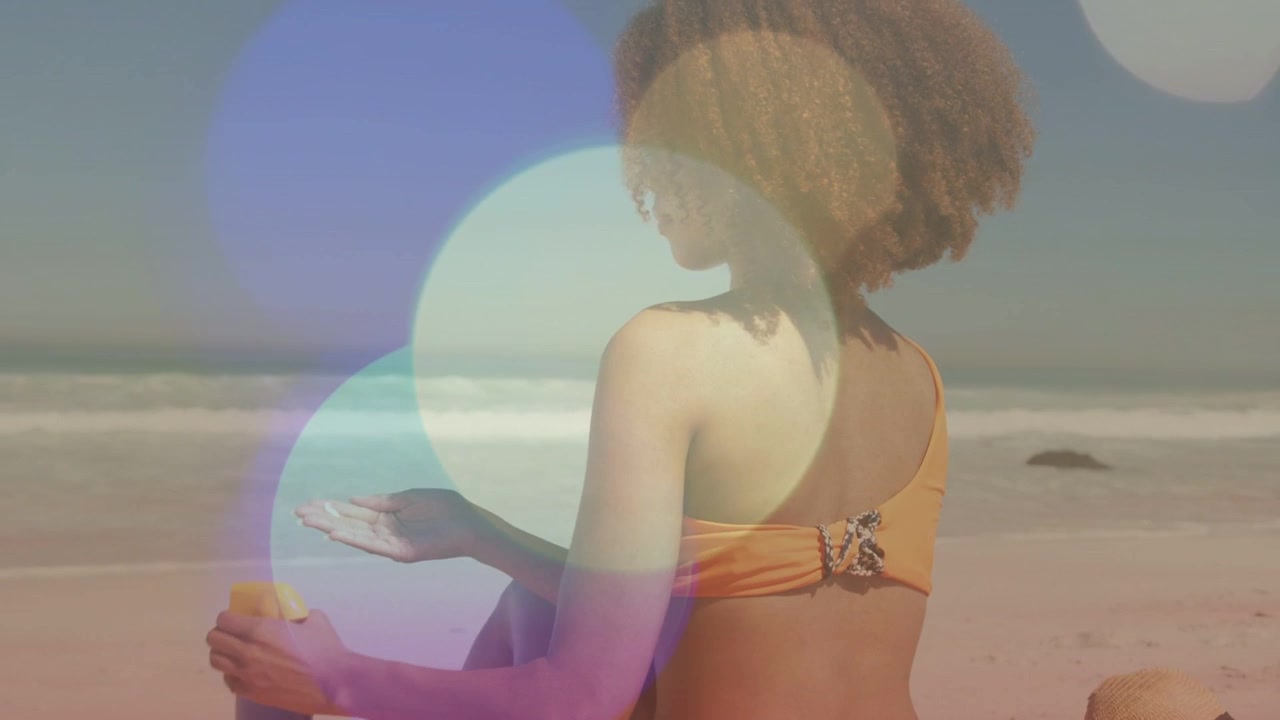 Woman opening SPF and pumping lotion, rubbing shoulder on beach towel with bokeh overlay drifting