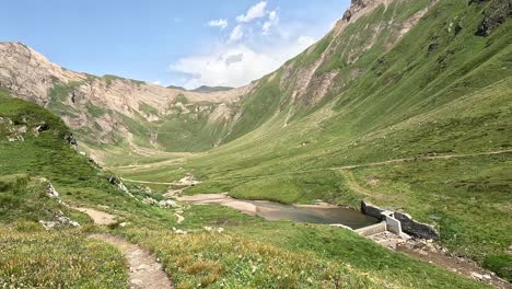 üppiges-Grünes-Bergtal-Mit-Einem-Kleinen-Fluss-Und-Einem-Damm