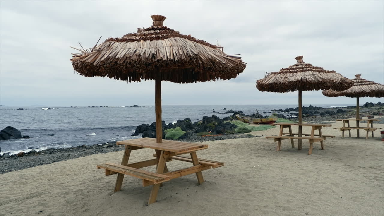 흐린 해변:  빈 피크닉 테이블 위에 잔디 우산, 사람 없음