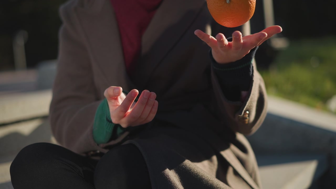 Person Tossing and Catching an Orange Outdoors