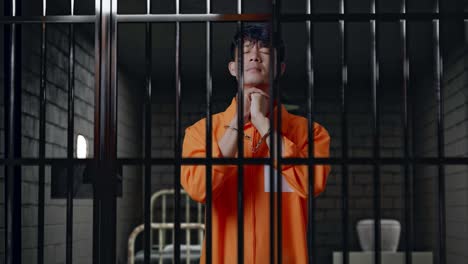 asian male prisoner in handcuffs prays for something while standing in prison