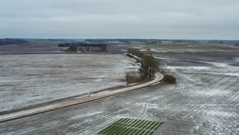 Fliegen-Sie-über-Eine-Schotterstraße-Auf-Dem-Land-Mit-Bäumen-Und-Gefrorenen-Getreidefeldern