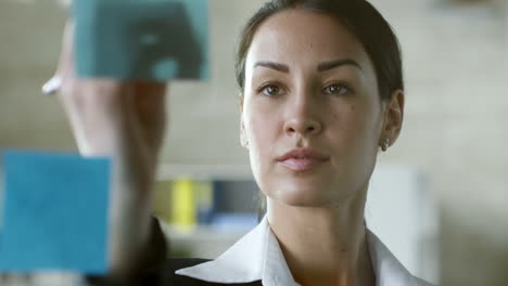 confident female entrepreneur using sticky notes attached to glass wall when planning work in office