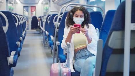 woman using mobile phone while traveling by train wearing a face mask