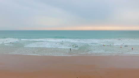 Hermosa-Puesta-De-Sol-Cielo-Color-Pastel-Sobre-Playa-De-Arena-Dorada-Y-Surfistas