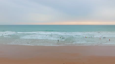 beautiful sunset pastel colored sky above golden sandy beach and surfers