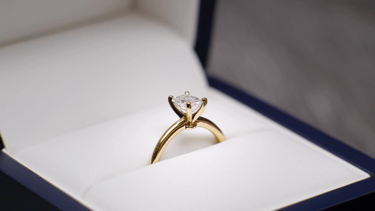 Anello di fidanzamento con diamante per proposta di matrimonio in una scatola che si apre. Anello di fidanzamento svelato. Diamante taglio smeraldo con bordo a lama di coltello in oro giallo
