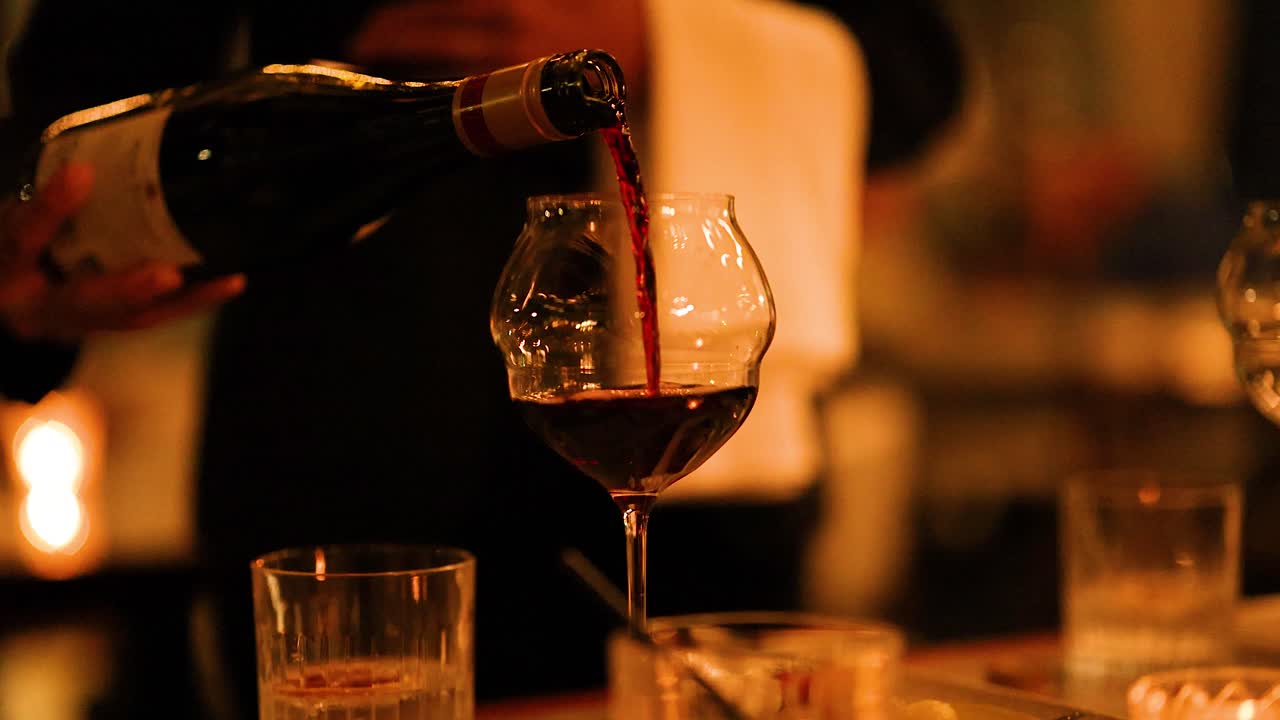 A wine bottle pours into a glass in a warm, intimate, candlelit environment, creating a sophisticated and inviting atmosphere
