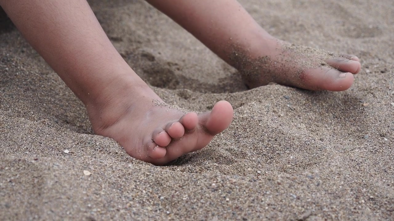 Bambino che muove le dita dei piedi nella sabbia in spiaggia