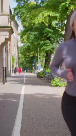 Vídeo-Vertical-De-Una-Mujer-Joven-Haciendo-Ejercicio-Mientras-Corre-Por-La-Acera-En-Una-Calle-De-La-Ciudad-Usando-Auriculares-Inalámbricos