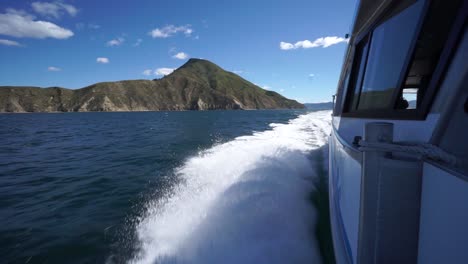 olas espumosas rompiendo en el costado del barco de crucero en los sonidos de marlborough, nueva zelanda con verdes colinas en el fondo