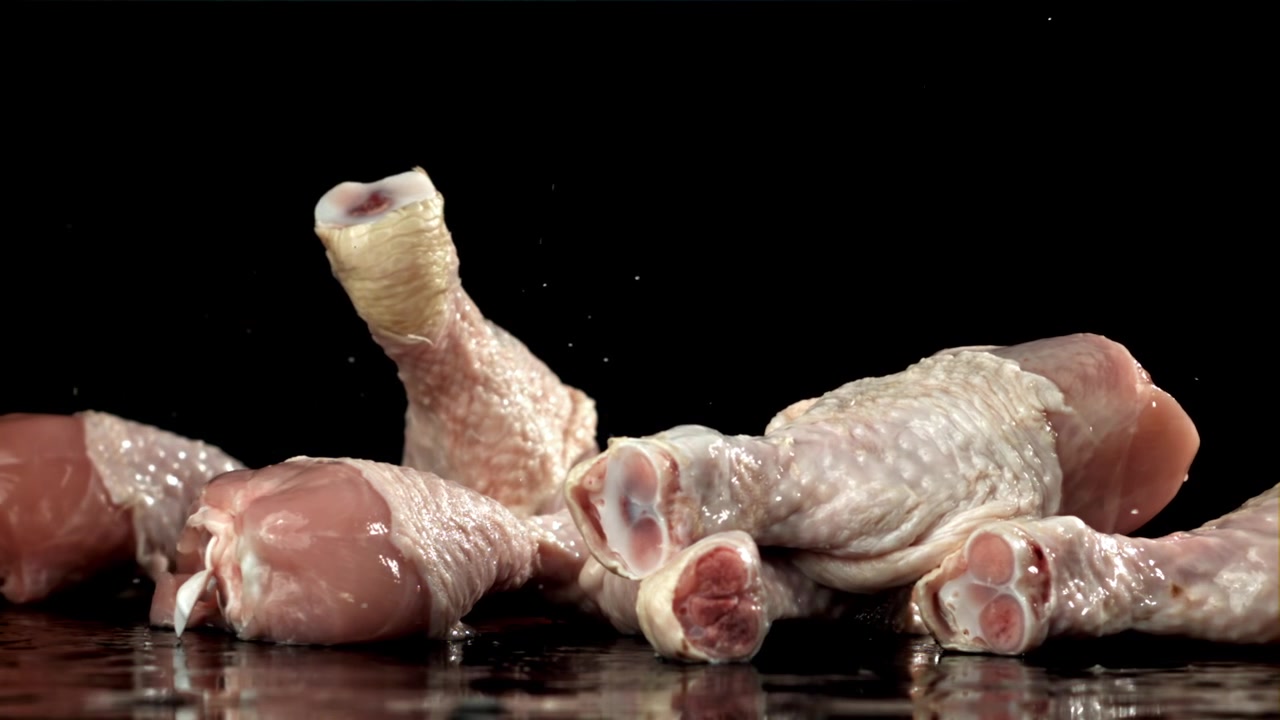Fusi di pollo crudi che cadono su una superficie nera bagnata in movimento rallentato