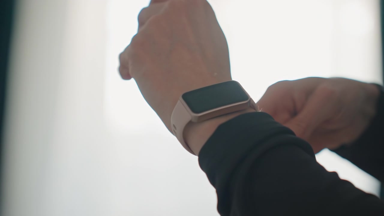 Closeup hands fastening smartwatch at home, soft bedroom light, neutral band, wrist adjustments before workout, quiet anticipatory mood, curtains backlit, wearable focus for fitness routine and health