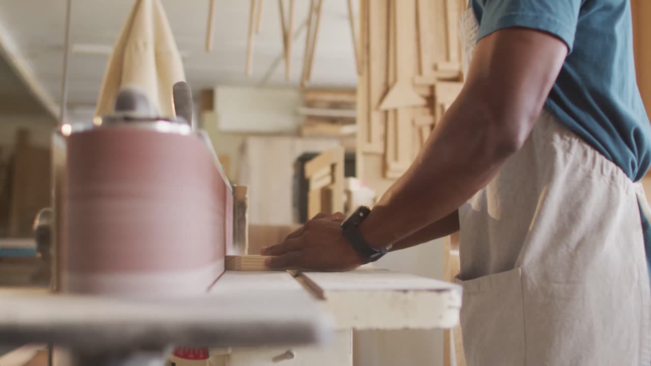 African american male carpenter wearing face mask using belt sander machine to polish wood