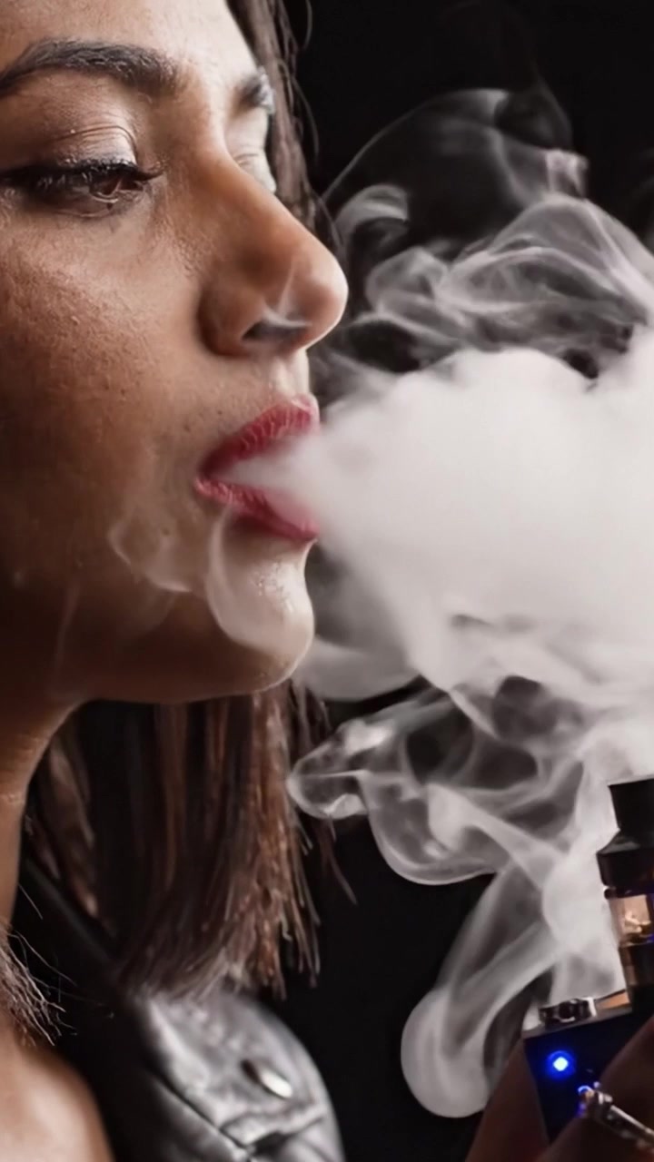 A Close-Up of a Woman Enjoying Vapor from a Modern Device, Capturing the Elegance of the Moment with Smoke and Style in a Dramatic Lighting Setting