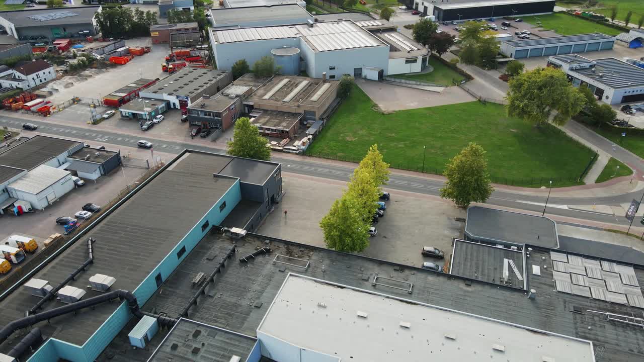 Aerial of a beautiful industrial zone with factories and warehouses. Green fields with trees are located between the buildings. Cars drive over the calm road on a sunny day