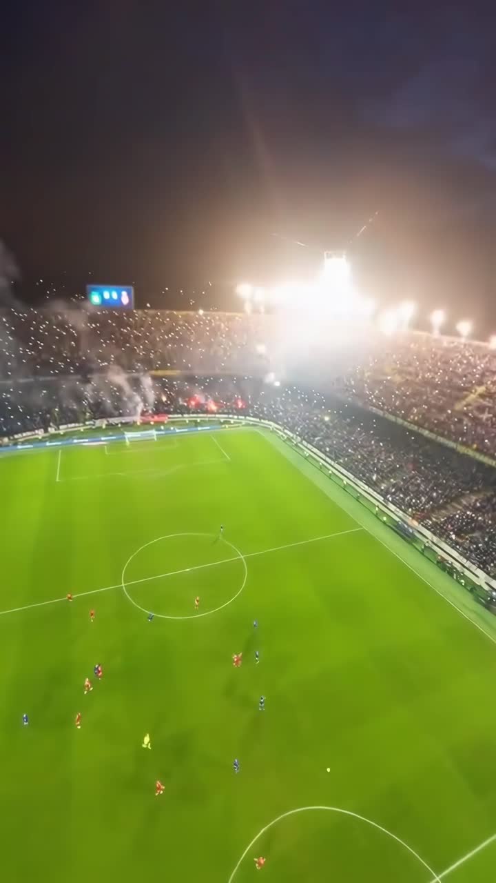 Ripresa video aerea di uno stadio di calcio vivace di notte, che cattura la dinamica partita sottostante.