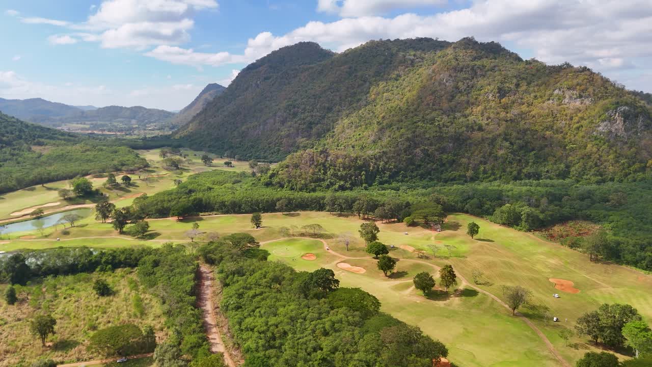Eine Drohnenaufnahme aus einem hohen Winkel fängt einen weitläufigen, grünen Golfplatz vor einer majestätischen Bergkulisse ein