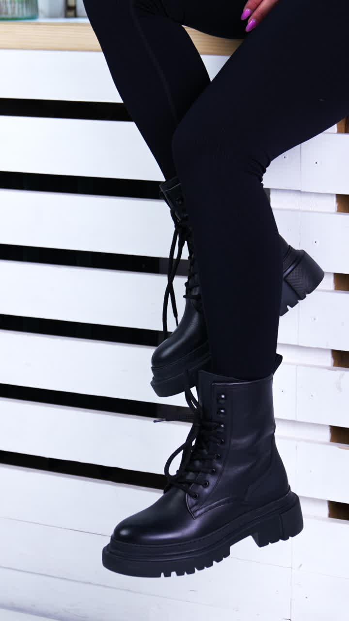 Female model sitting on the widow-sill demonstrating her footwear. Lady in black pants shows the black tractor boots with laces. Vertical video