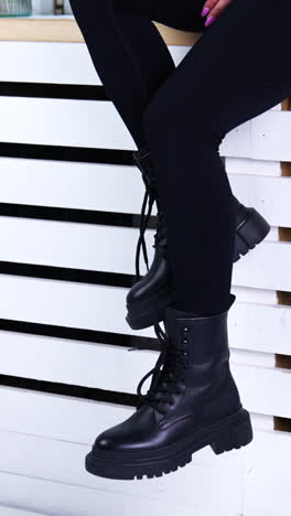 female model sitting on the widow-sill demonstrating her footwear. lady in black pants shows the black tractor boots with laces. vertical video