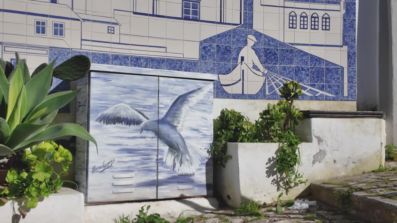 Street art depicting a seagull flying over the water in Ferragudo, Portugal, with traditional portuguese tiles in the background