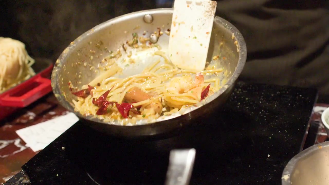 Un primo piano di uno chef che salta gli spaghetti in una padella su un piano cottura a induzione.
