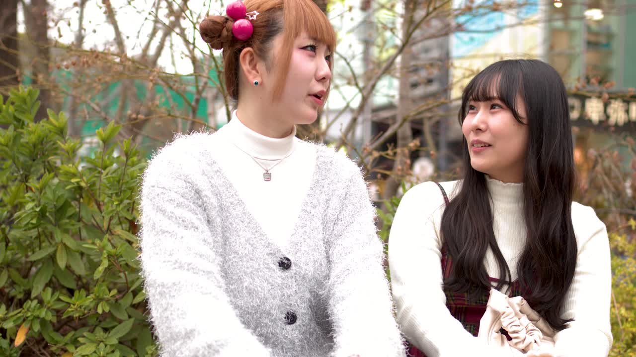 東京の屋外で、おしゃれな原宿ファッションに身を包んだ若い女性2人が笑いながら話している