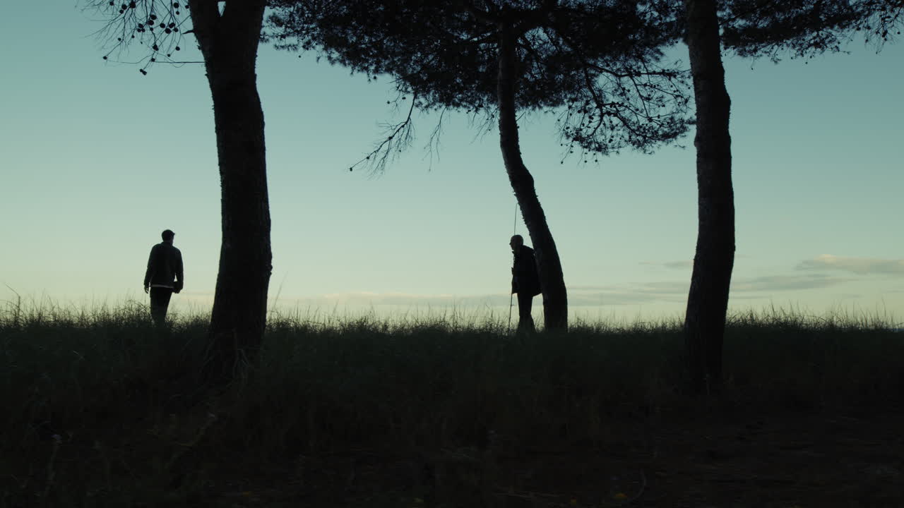 Silhouette Of Two People Walking Among Forest Trees In The Morning Near The Sea