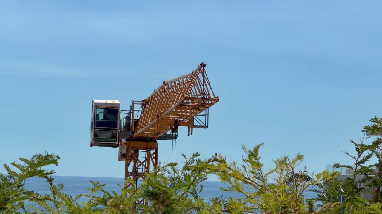 A construction crane in a coastal city building a plush house against the mountains
