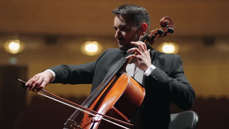 musician in black suit is playing cello on scene of opera house symphonic orchestra in philharmonic hall