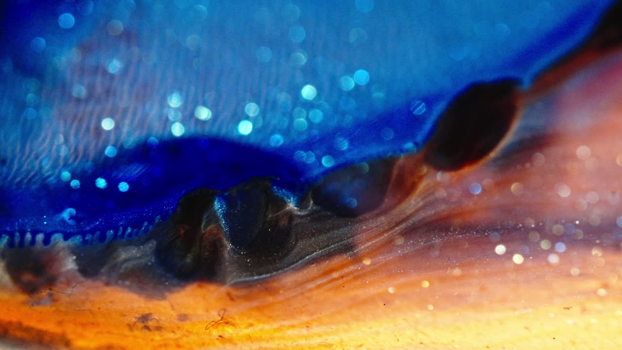 Swirling colorful liquids blend together with glittering particles in a macro view, abstract shot