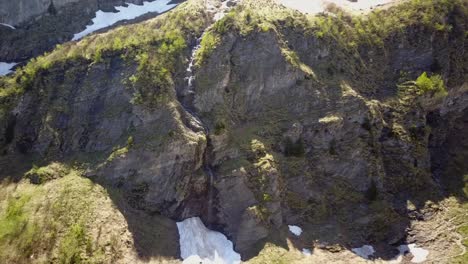 Alejarse-De-Una-Cascada-En-Los-Alpes-Suizos,-Con-Algo-De-Nieve-Alrededor