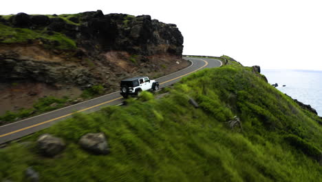 aerial view, jeep drives around cliff on maui coastline, hawaii.